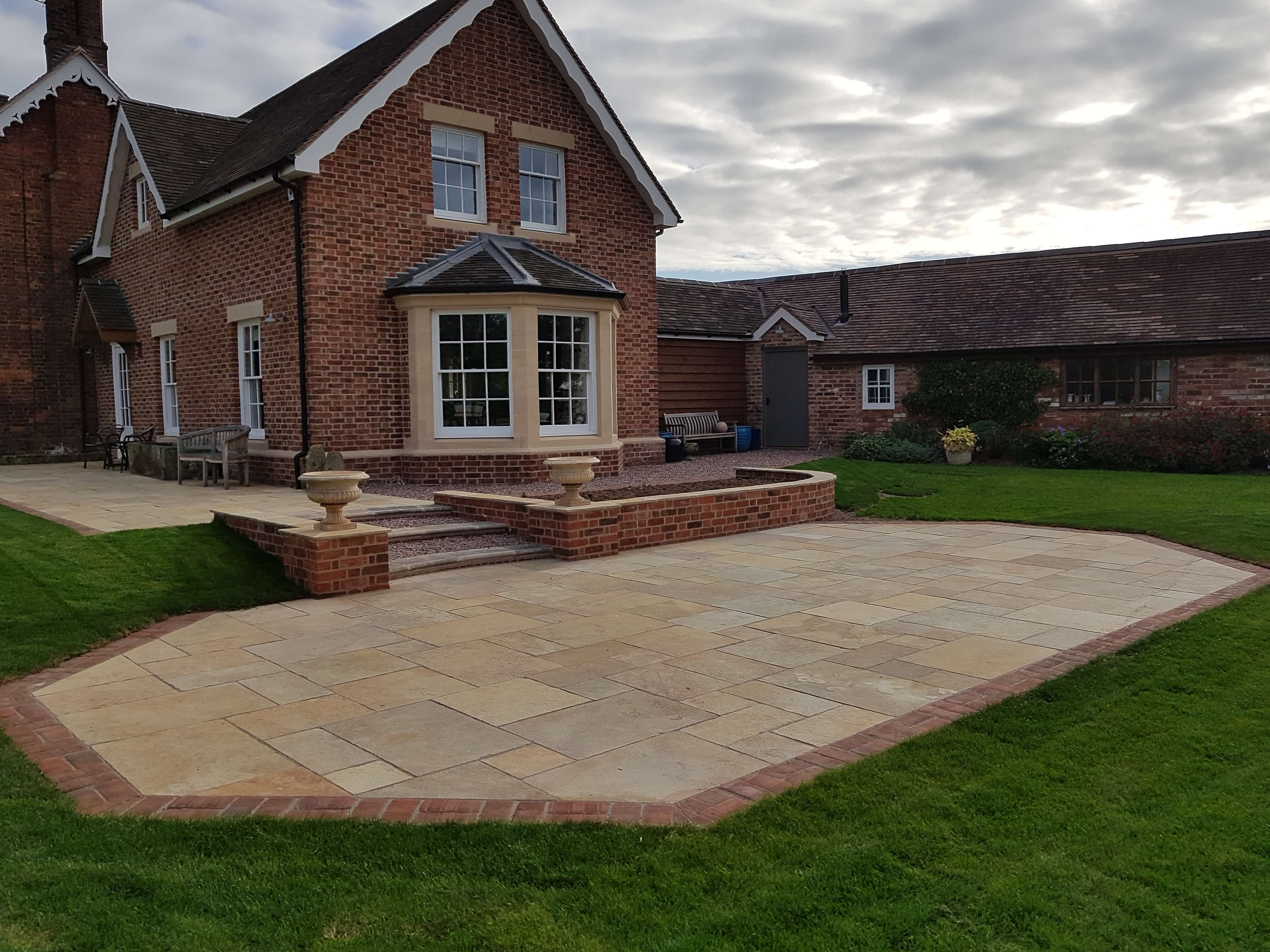 Large sandstone patio with brick edging and raised steps